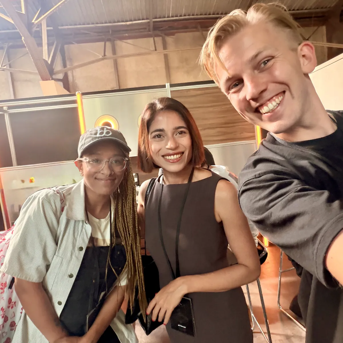 Selfie of Jono, Sne and Bersabel Tadesse from BB, who is wearing a cap and glasses, at a booth inside the venue