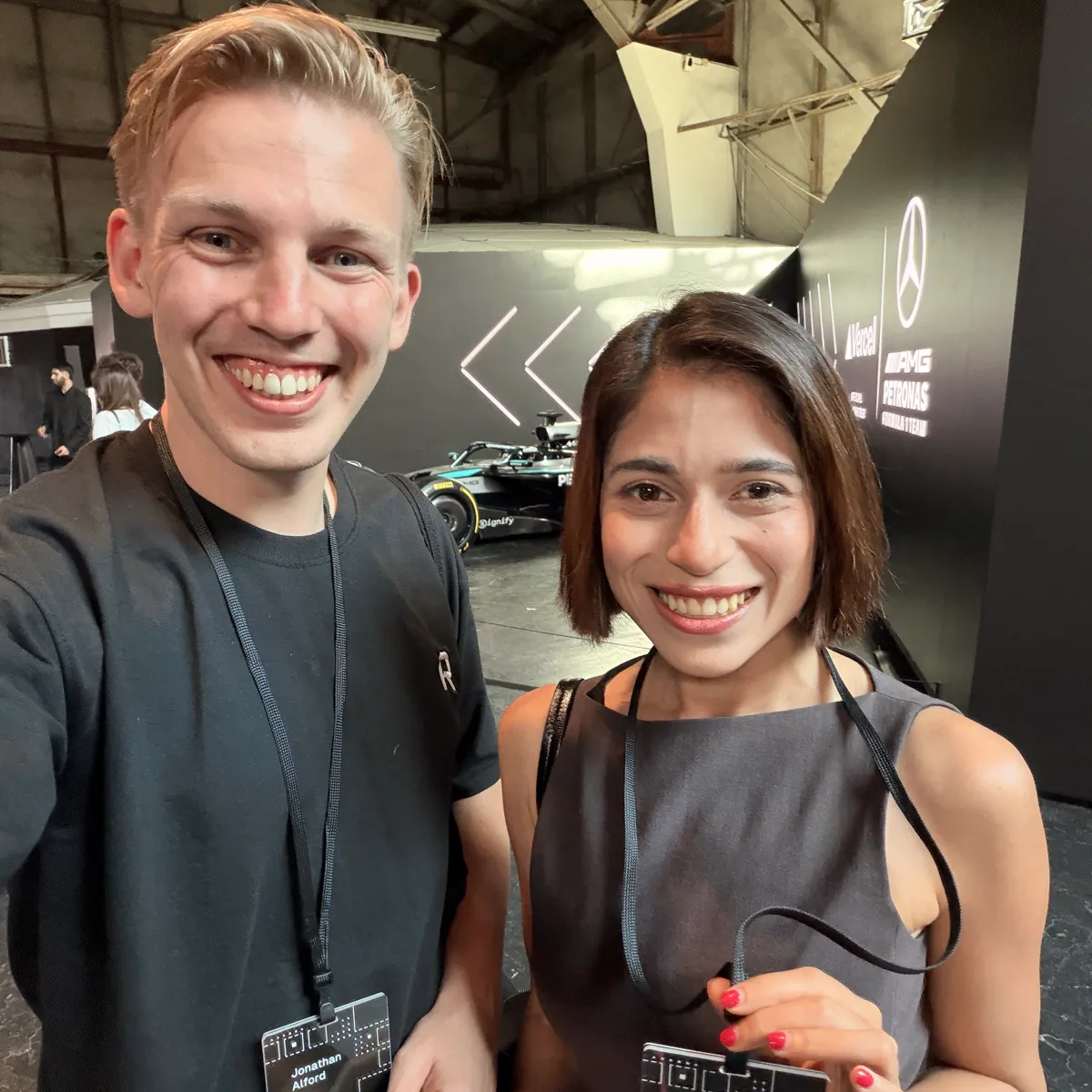 Jono and Sne wearing Ship badges that read Jonathan Alford, Founder, and Snehil Tripathi, Account Exec, Roboto Studio, in front of a Mercedes AMG Petronas F1 car