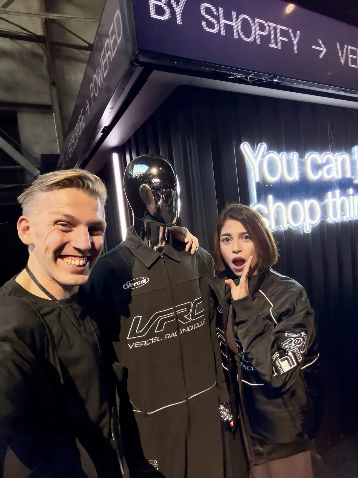 Jono and Sne, wearing the Vercel Racing Club bomber jacket, either side of a chrome mannequin in the matching racing suit at the Vercel store powered by Shopify